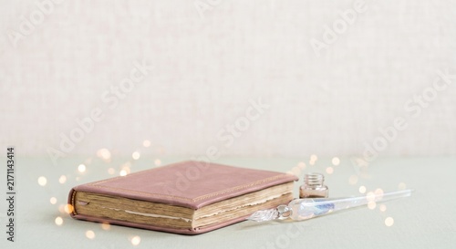 Aesthetic still life: vintage pink leather journal, glass dip pen, and ink bottle with glowing fairy light bokeh