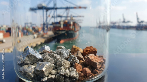 Rare earth supplies in glass bowl beside blurred cargo ship and industrial harbor create reflective scene about mineral resources, global trade, and environmental responsibility