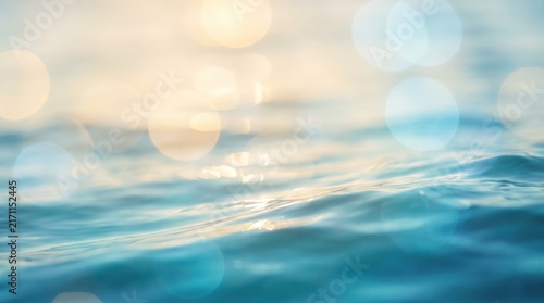 Sun rays reflecting on blue ocean waves creating a soft golden bokeh background.