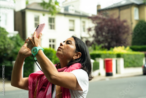 Canvas Print Woman standing on a London street, using a mobile phone to photograph buildings