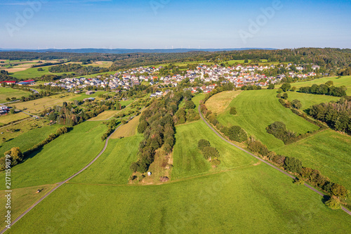 A bird's-eye view of a small village in the Taunus Mountains, surrounded by fields, meadows, and forests.