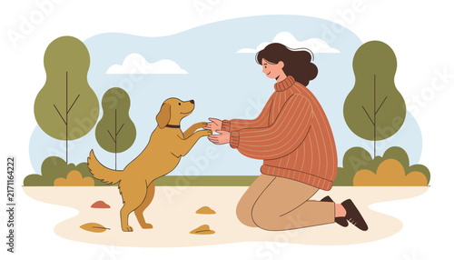 Caring young woman kneeling in an autumn park and holding paws with her friendly golden retriever dog companion.
