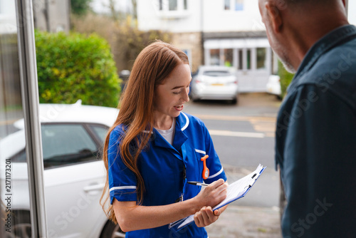 Nurse visits a home and takes notes while speaking to a patient outside