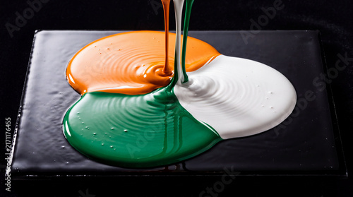 Vibrant orange, white, and green liquid paint drops flowing and overlapping on a dark surface, creating a colorful abstract composition for creative backgrounds and design projects.