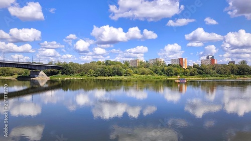 Foto Photo of the Vistula river beneath a brilliant blue summer sky dotted with fluffy clouds, with the Ślasko-Dabrowski bridge and the apartment buildings of Stara Praga neighborhood lining the riverbank
