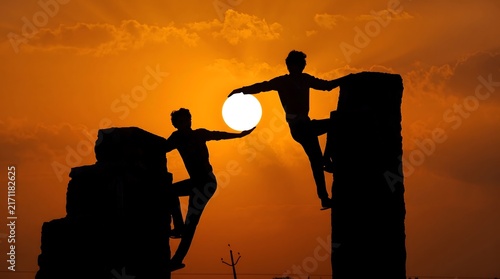 Silhouette of two men climbing walls while passing the sun with adventure together mountain strength