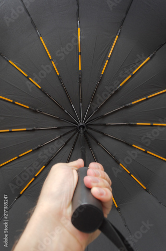 Hand holding black umbrella with orange accents, low angle view from below