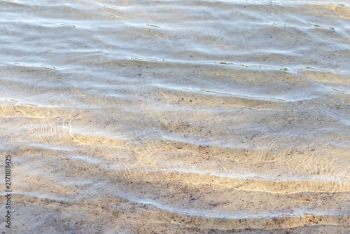 Принти на полотні Shallow clear water laps over a sandy beach, forming gentle ripples and sunlit reflections on the seabed