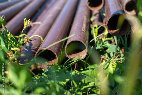 Fotografía Old rusty steel pipes lying on ground in grass close up