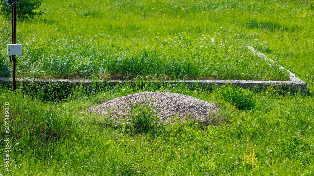 Naklejka premium Gravel mound sits in green grass. Concrete foundation lies nearby. Grass grows around construction site.