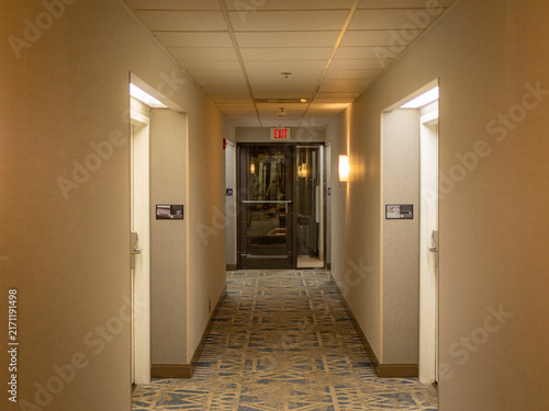 Konstfotografi A symmetrical view down a well lit indoor hotel hallway with patterned carpet, c