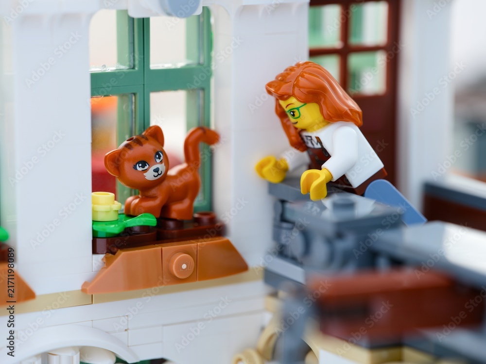 Fototapeta premium Tambov, Russian Federation - August 22, 2026 A close-up shot of a Lego woman minifigure reaching out to rescue a ginger cat from a window sill.