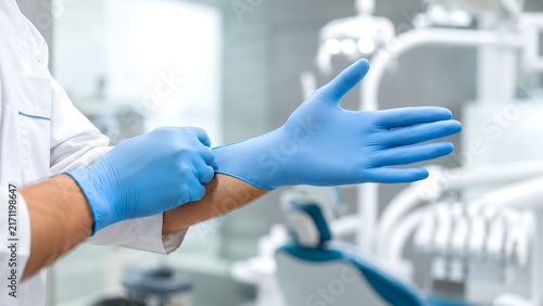Dentist putting on blue protective gloves in modern dental clinic for hygiene and infection control