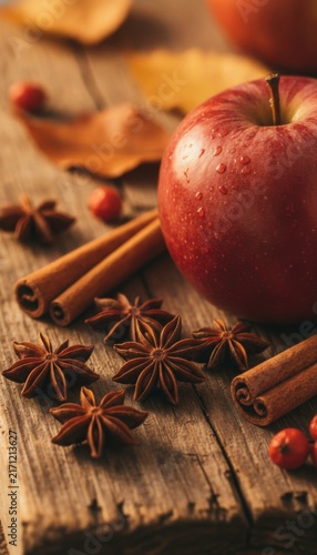 Red apple, star anise, and cinnamon sticks on rustic wooden background with autumn leaves, concept of autumn flavors and cozy comfort