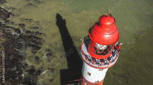 Photography Iconic red and white lighthouse casting a long shadow over the murky sea