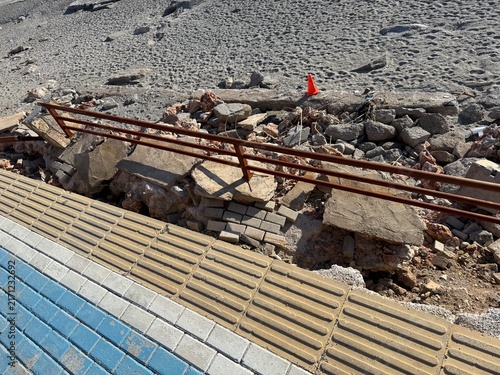 Canvastavla Broken walkway with damaged railing and rubble near sandy beach under bright sun