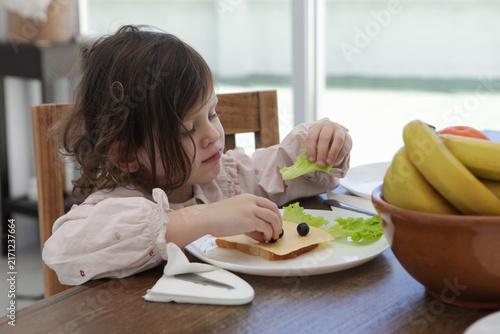 Canvastavla A little girl places blueberries onto a slice of toast on her plate during a healthy breakfast or lunch routine at home