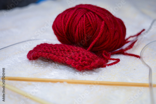 Принти на полотні Ball of red wool yarn with a knitted swatch and wooden circular knitting needles on a soft white background close-up