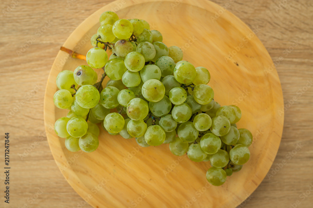 Naklejka premium Fresh green grapes on a round wooden plate, shot from above on a light wood surface. Perfect for healthy eating and organic food concepts