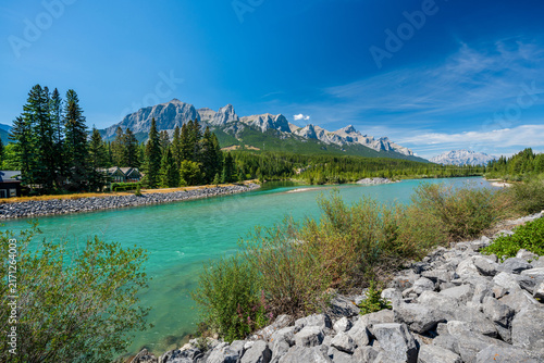 Summer landscape of Bow River turquoise water and waterfront cabins against Mount Rundle. Canmore, Alberta, Canada.