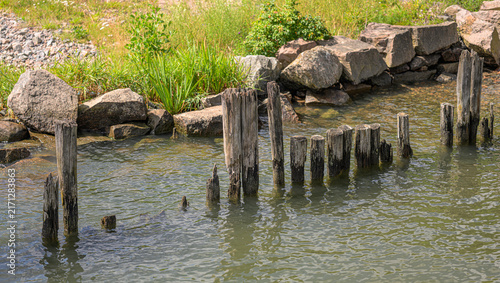 Canvastavla Weathered wooden pilings remain in rocky urban shoreline water.