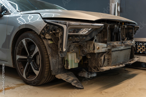 Fotografía Car front corner rests in workshop with silver body panel, exposed headlamp housing, and missing bumper cover