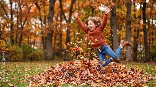 Joyful young girl jumping into a pile of autumn leaves in a forest setting