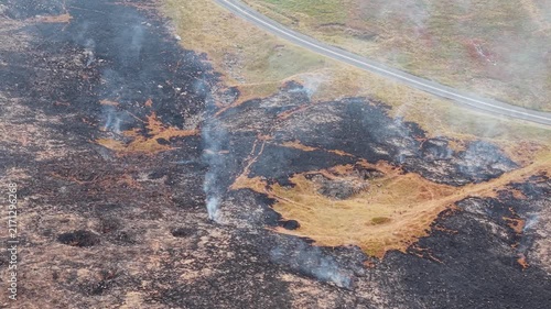 Wisps of smoke drifting from smouldering peatland post moorland fire, charred heather and blackened vegetation covering hill slope
