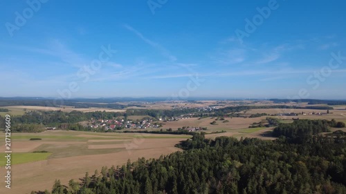 Aerial view of a bright rural landscape in sunny weather, featuring lush green vegetation, open countryside and winding roads surrounded by natural scenery.