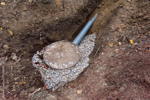 Improvised barrel septic tank with gravel drainage and a PVC pipe in a dirt trench
