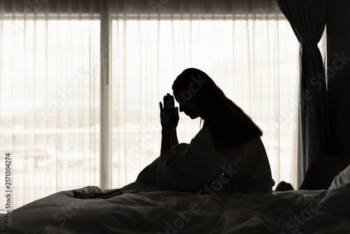 Obraz na plátně Woman Saying a Prayer While Sitting on Bed in Silhouette