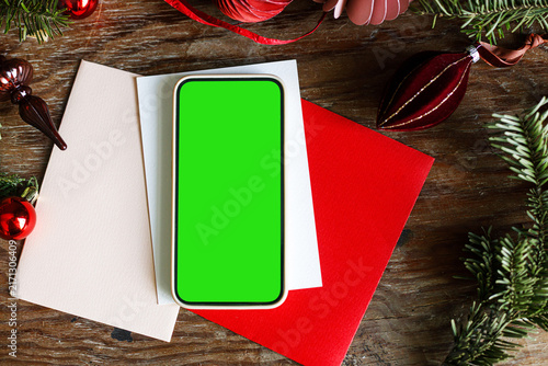Obraz na plátně Smartphone with green screen chroma key mockup on Christmas envelopes and wooden background