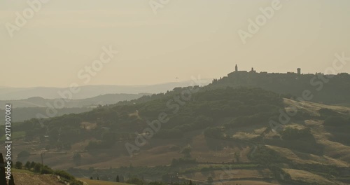 Paraglider flying over the Tuscan countryside with Pienza on the horizon in Val d'Orcia, Italy