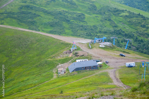 High angle summer view of Dragobrat, Ukraines highest ski resort, showing a chairlift station on Mount Stig, a winding dirt road, and vibrant green mountain ridges under an overcast sky