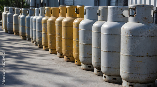 Perspective view of weathered gray and yellow gas cylinders lined up in a long row on a textured concrete surface, with generous copy space emphasizing industrial storage, energy supply, logistics, 