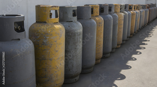 Perspective view of weathered gray and yellow gas cylinders lined up in a long row on a textured concrete surface, with generous copy space emphasizing industrial storage, energy supply, logistics, 