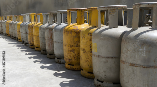 Perspective view of weathered gray and yellow gas cylinders lined up in a long row on a textured concrete surface, with generous copy space emphasizing industrial storage, energy supply, logistics, 