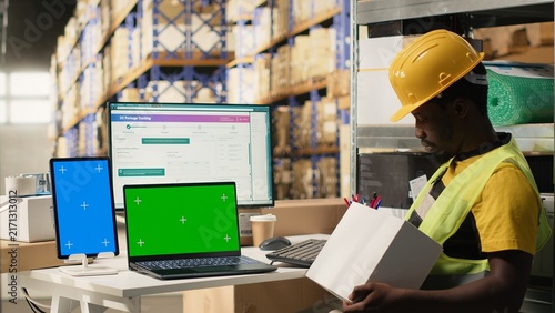 Fotografie African American worker follows shipments with tracking information beside copy space in a warehouse with organized shelving and pallets for timely dispatch