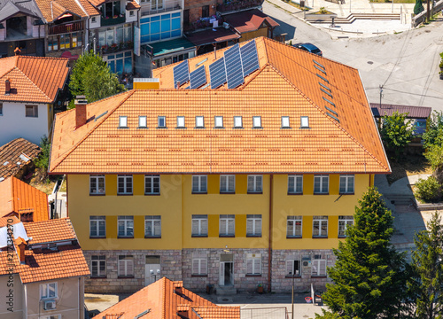 Aerial view of a yellow building with a terracotta tiled roof, solar panels, and stone foundation in Vevchani, Vevcani Municipality, North Macedonia.