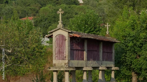 Espigueiro raised on stone pillars with wooden slats and carved crosses among green hillside trees
