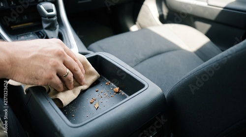 Hand wiping crumbs from car center console storage tray