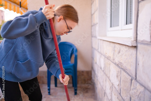 Teenage girl cleaning a balcony floor with a broom.