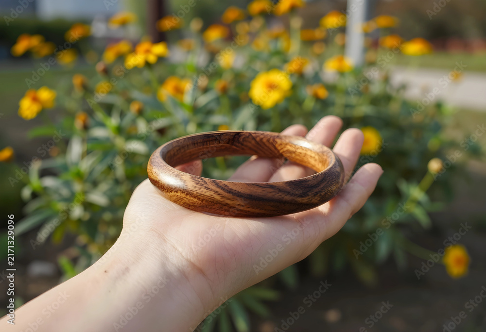 Naklejka premium Hand holding a natural wooden bangle bracelet, sustainable fashion and eco-friendly jewelry concept outdoors