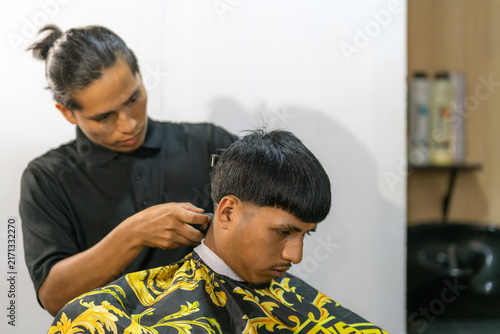 Barber trimming client's hair in barbershop