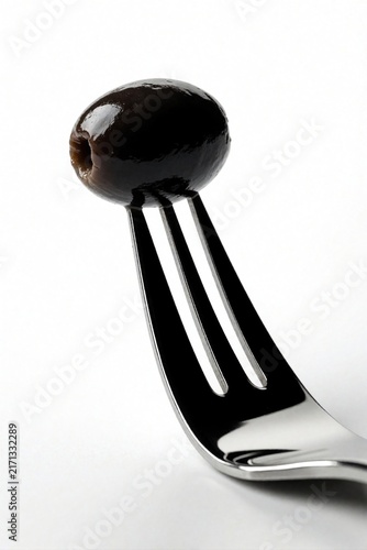 Single black olive impaled on silver fork. Simple minimalist food shot against clean white backdrop. Healthy snack or ingredient presentation.