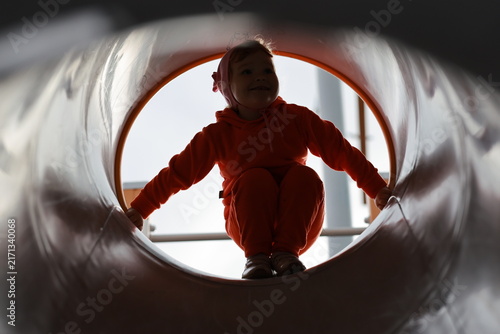 A happy child sliding through a tubular tunnel on a playground transitions from a squatting position to a sitting position during active children's play and leisure.
