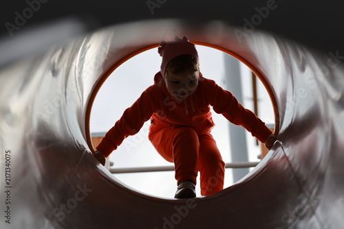 A happy child sliding through a tubular tunnel on a playground transitions from a squatting position to a sitting position during active children's play and leisure.
