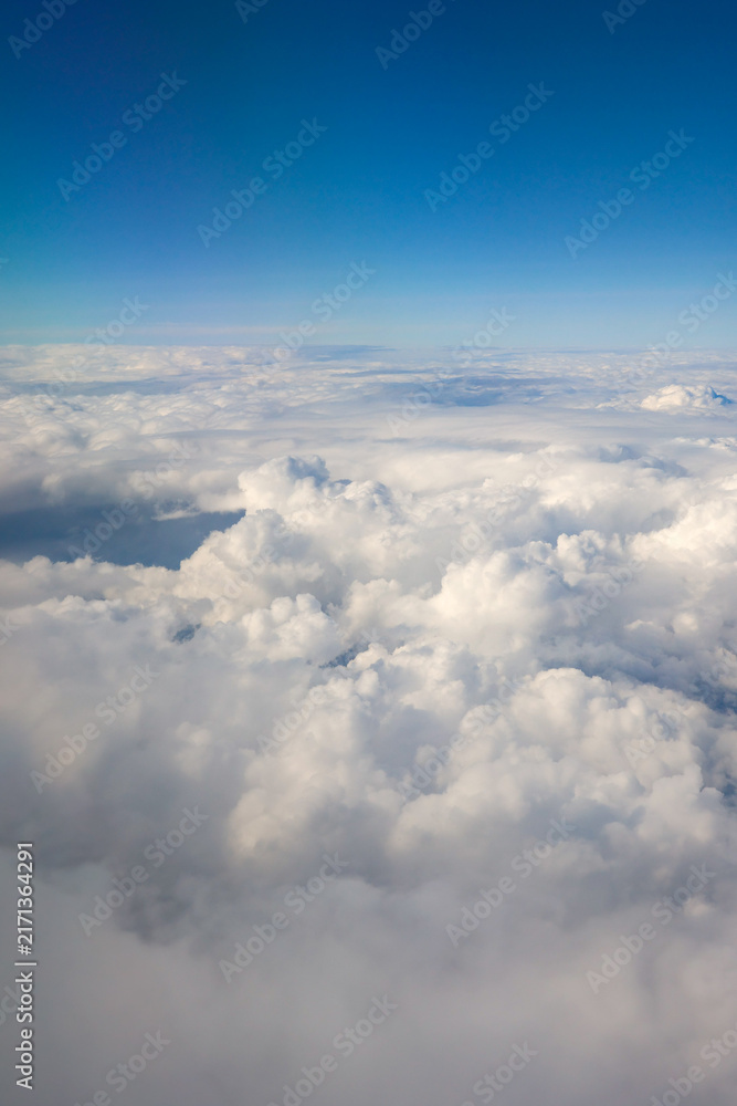 Fototapeta premium White fluffy cumulus clouds extend to the horizon under a clear blue sky, forming a serene cloudscape from an aerial perspective