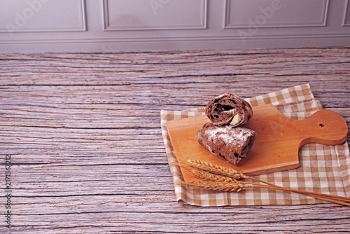 Sliced sourdough rests on a wooden board. Flour dusted loaf shows soft, chewy interior. Two wheat stalks add rustic charm. Checkered cloth beneath board enhances warmth. Ideal for food, bakery