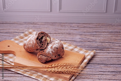 Sliced sourdough rests on a wooden board. Flour dusted loaf shows soft, chewy interior. Two wheat stalks add rustic charm. Checkered cloth beneath board enhances warmth. Ideal for food, bakery